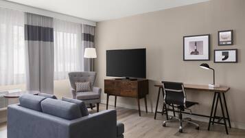 A modern hotel room with a sofa, a desk with a computer, a TV, and a chair.