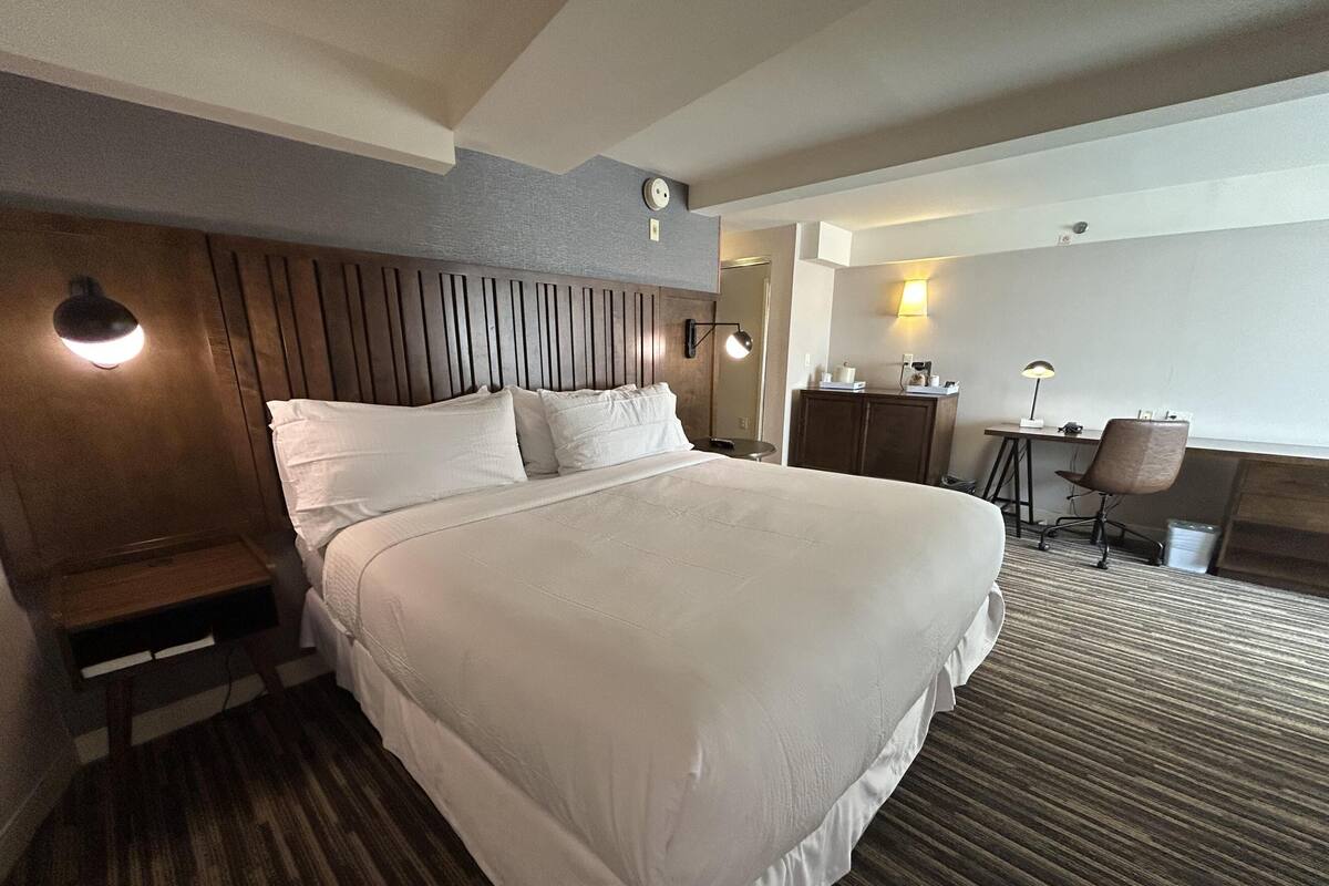 A hotel room with a large bed, a desk, a chair, and a small table.