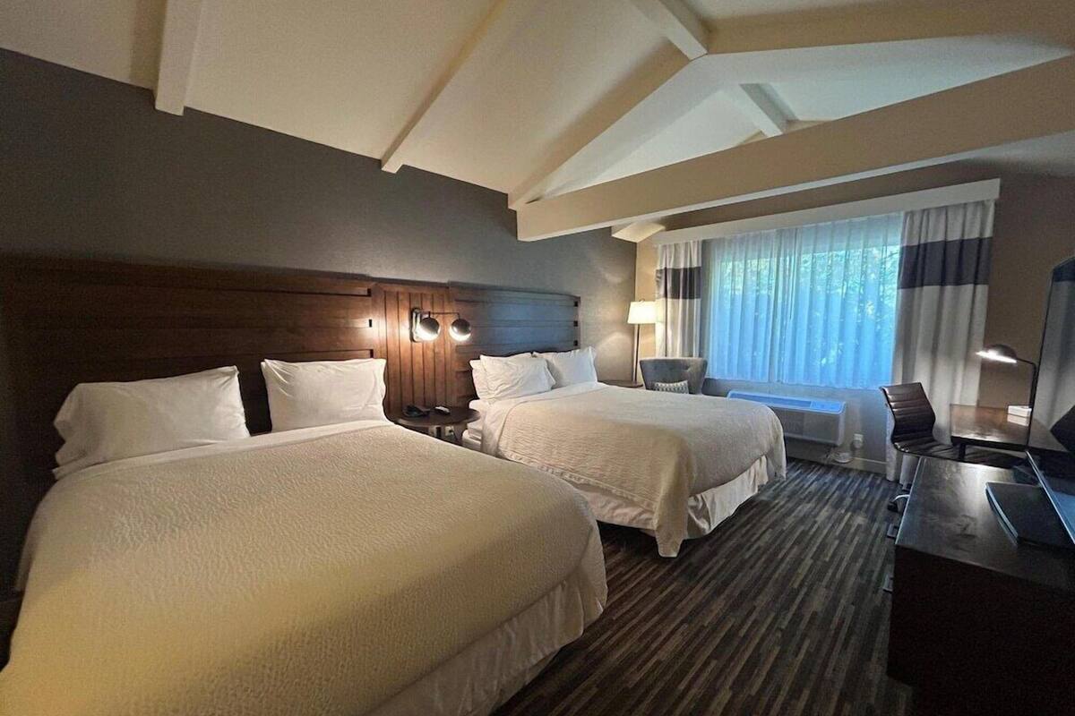 A hotel room with two beds, a desk, a chair, and a large window with curtains.