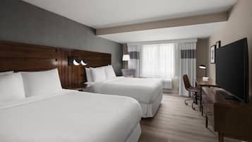 A hotel room with two beds, a desk, a chair, a TV, and a window with curtains.