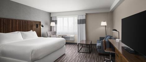 Una habitación de hotel con una cama grande, un escritorio, una silla, un televisor y una ventana con cortinas.