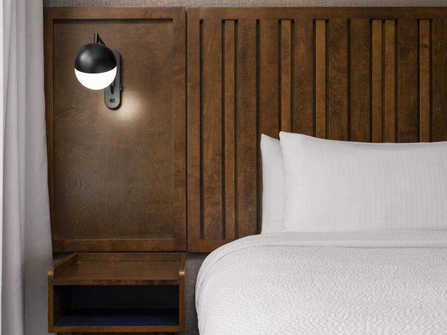 A hotel room with a wooden headboard, a bedside table, a lamp, and a bed with white bedding.