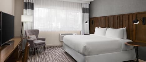 Une chambre d’hôtel avec un lit, un bureau, une chaise, une télévision et une lampe.