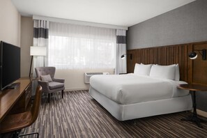 Een hotelkamer met een bed, bureau, stoel, televisie en lamp.