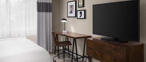 Una habitación de hotel con cama, escritorio con silla, televisor y una obra de arte en la pared.
