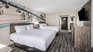 A hotel room with two beds, a TV, a desk, and a wall mural of bicycles.