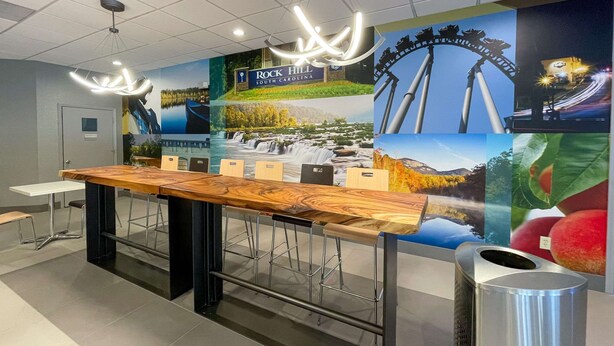 A reception area with a long wooden reception desk, metal bar stools, and a large wall mural depicting scenic views and the Rock Hill sign.