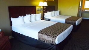 A hotel room with two beds, each with white linens and a patterned throw. There are two wall-mounted lamps above the beds.
