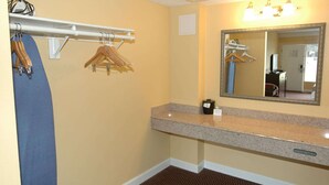 A hotel bathroom with a granite countertop, a mirror, and a towel rack with hangers.
