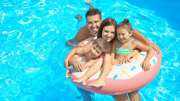A family in a swimming pool with a pink inflatable raft.