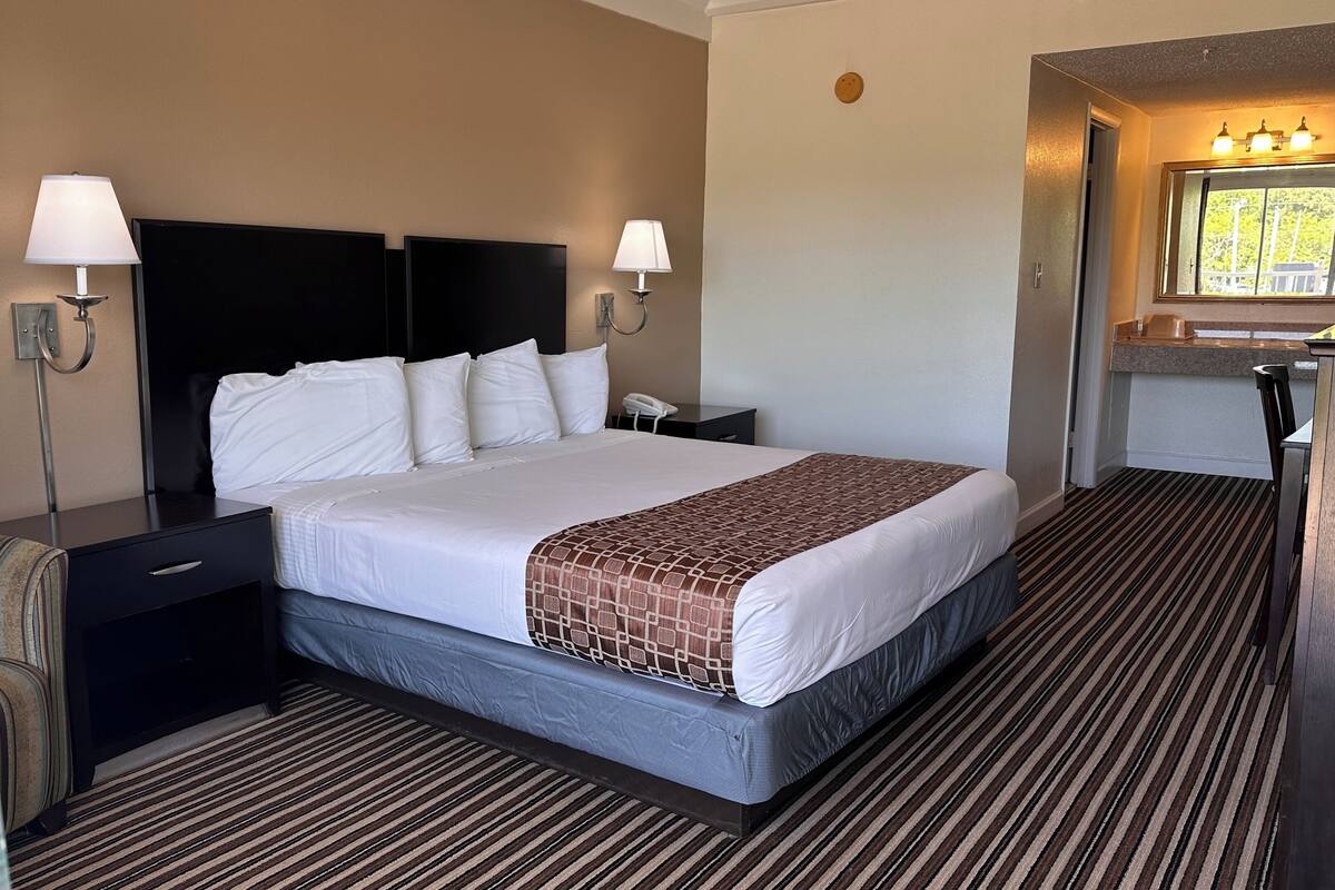 A hotel room with a bed, bedside tables, a desk, a mirror, and a window.