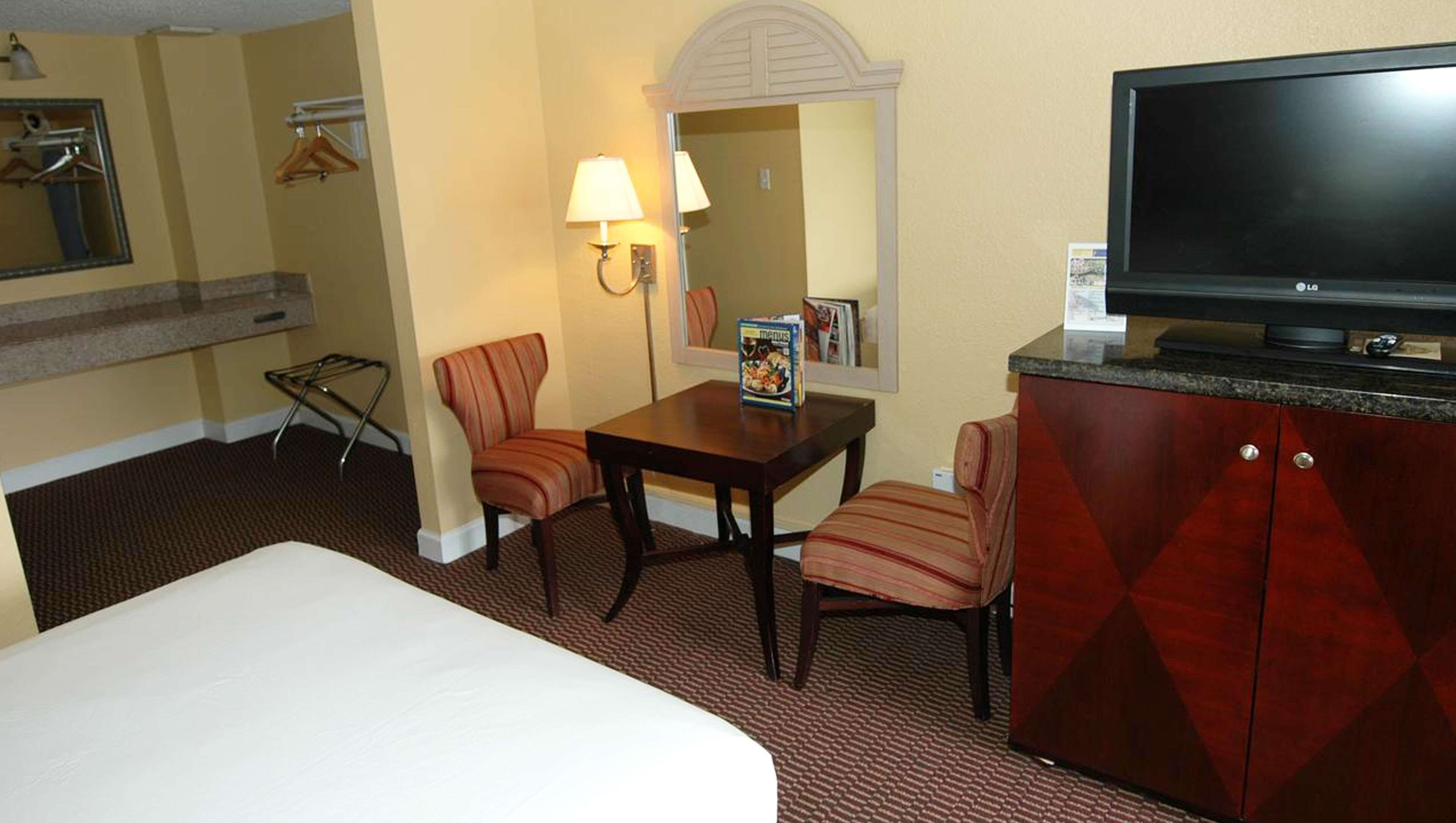 A hotel room with a bed, a desk with a chair, a television, a mirror, and a wardrobe.