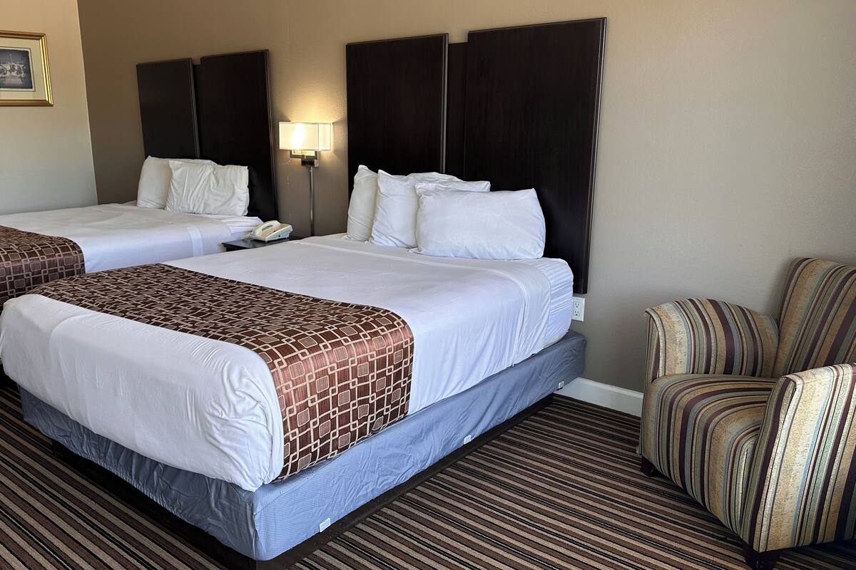 A hotel room with two beds, a striped armchair, and a bedside table with a lamp.