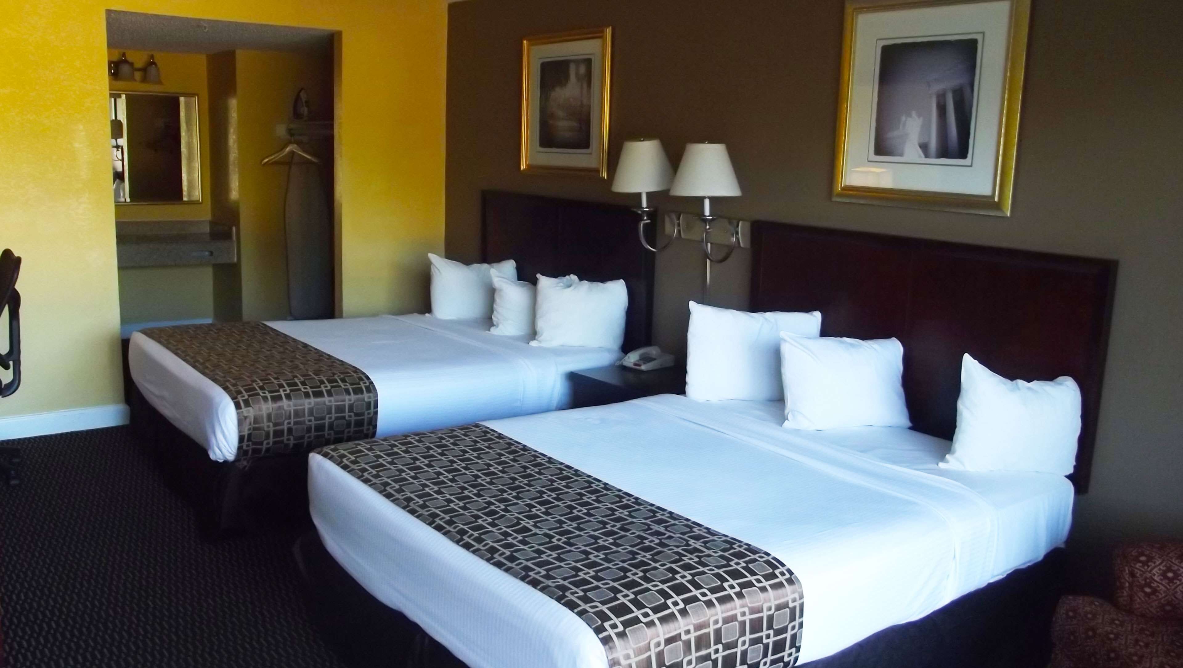 A hotel room with two beds, a mirror, a phone, and two wall-mounted lamps.