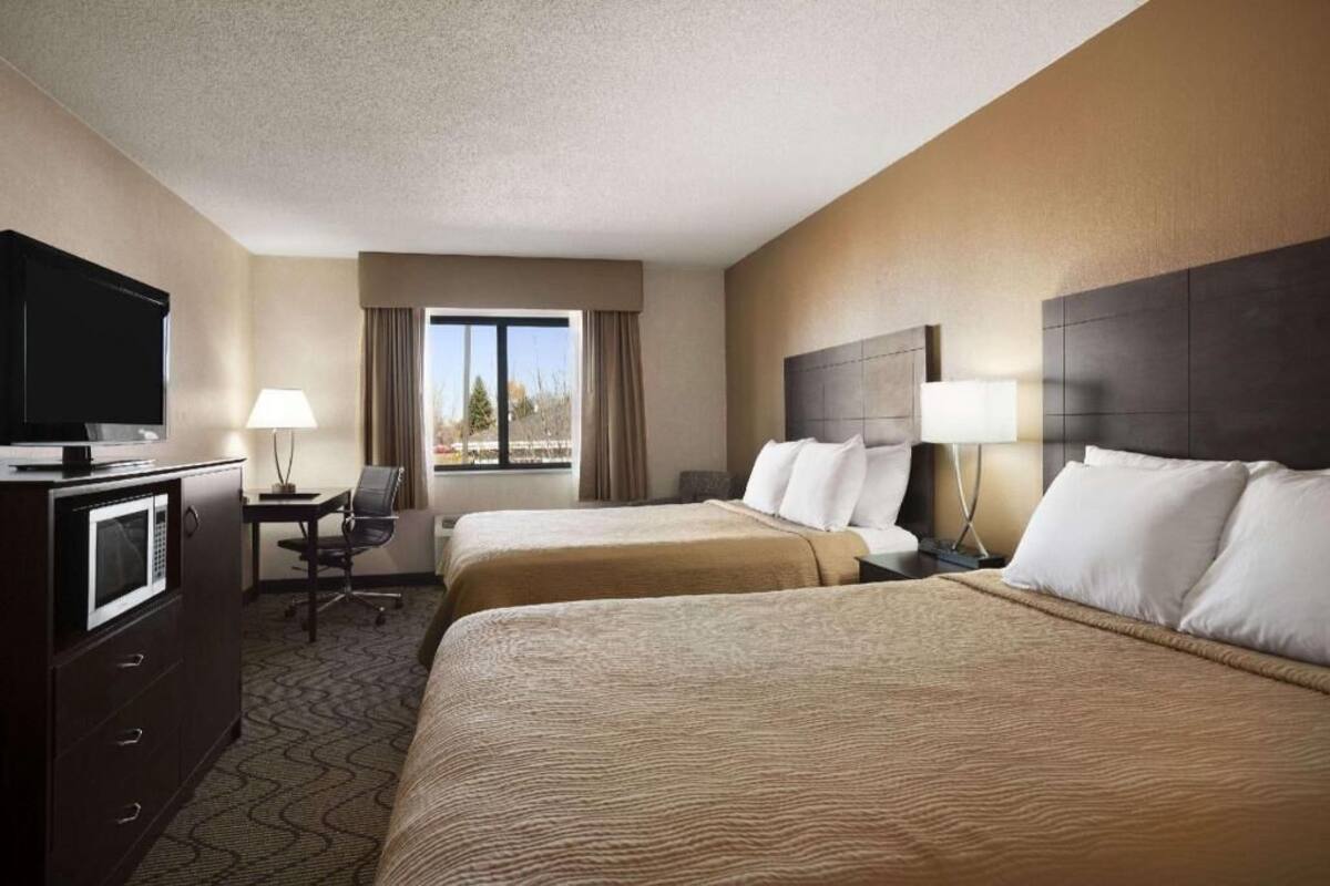 Habitación de hotel con dos camas, un escritorio, un televisor y una ventana con cortinas.