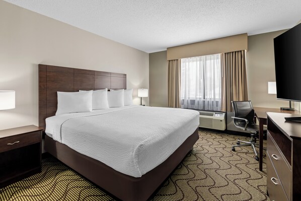 A hotel room with a large bed, a desk, a chair, an air conditioning unit, and a television. - Days Inn by Wyndham Grand Forks Columbia Mall (Grand Forks)