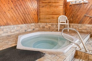 A hot tub with a stone surround, wooden walls, and a white chair. - Days Inn by Wyndham Grand Forks Columbia Mall (Grand Forks)