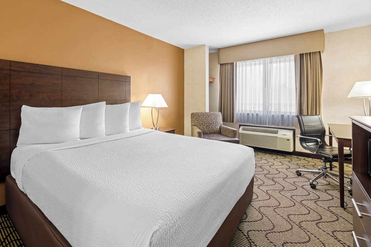 Habitación de hotel con una cama grande, un escritorio con silla, un equipo de aire acondicionado y una ventana con cortinas.