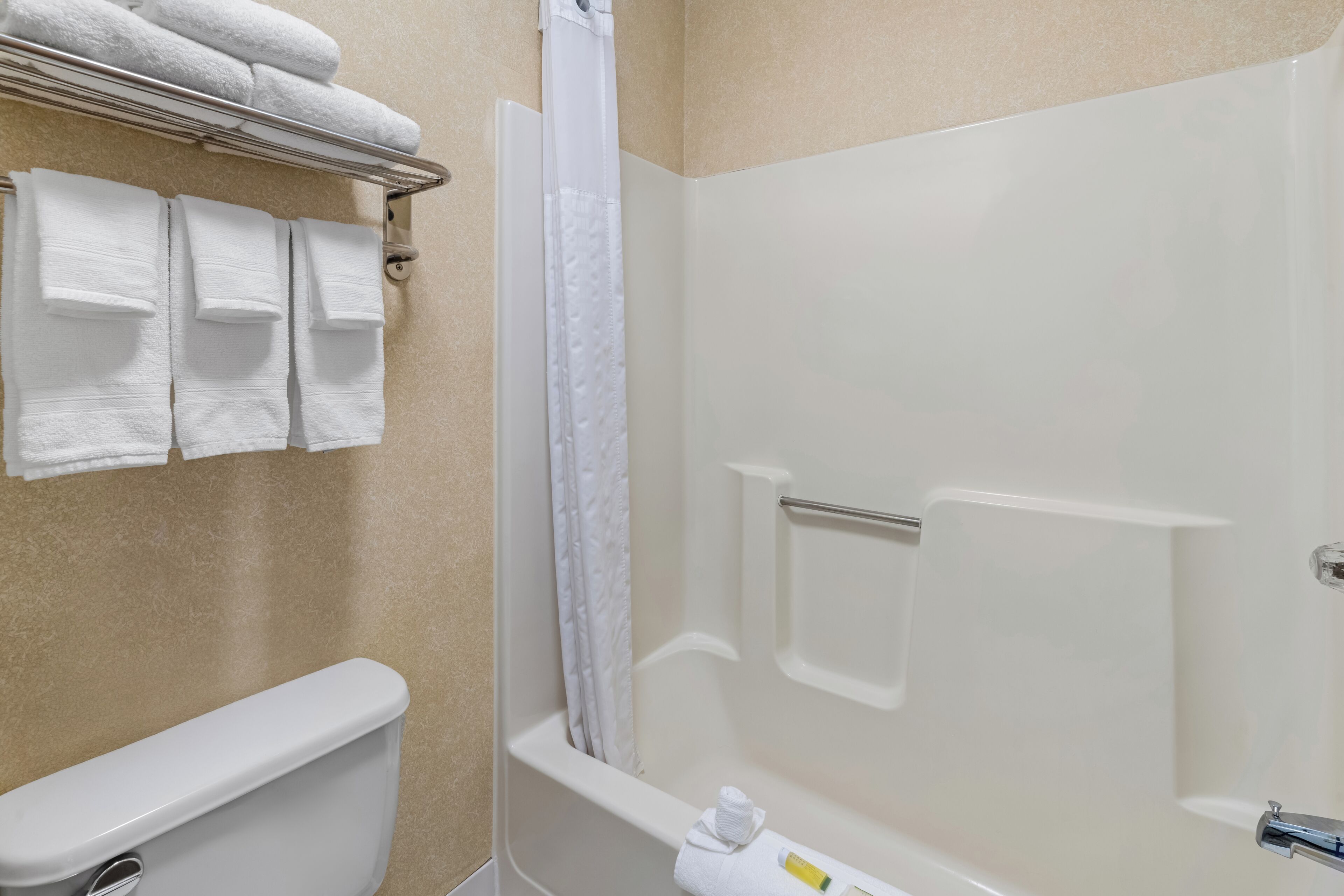 A bathroom with a toilet, a shower with a glass door, and a towel rack with folded towels.