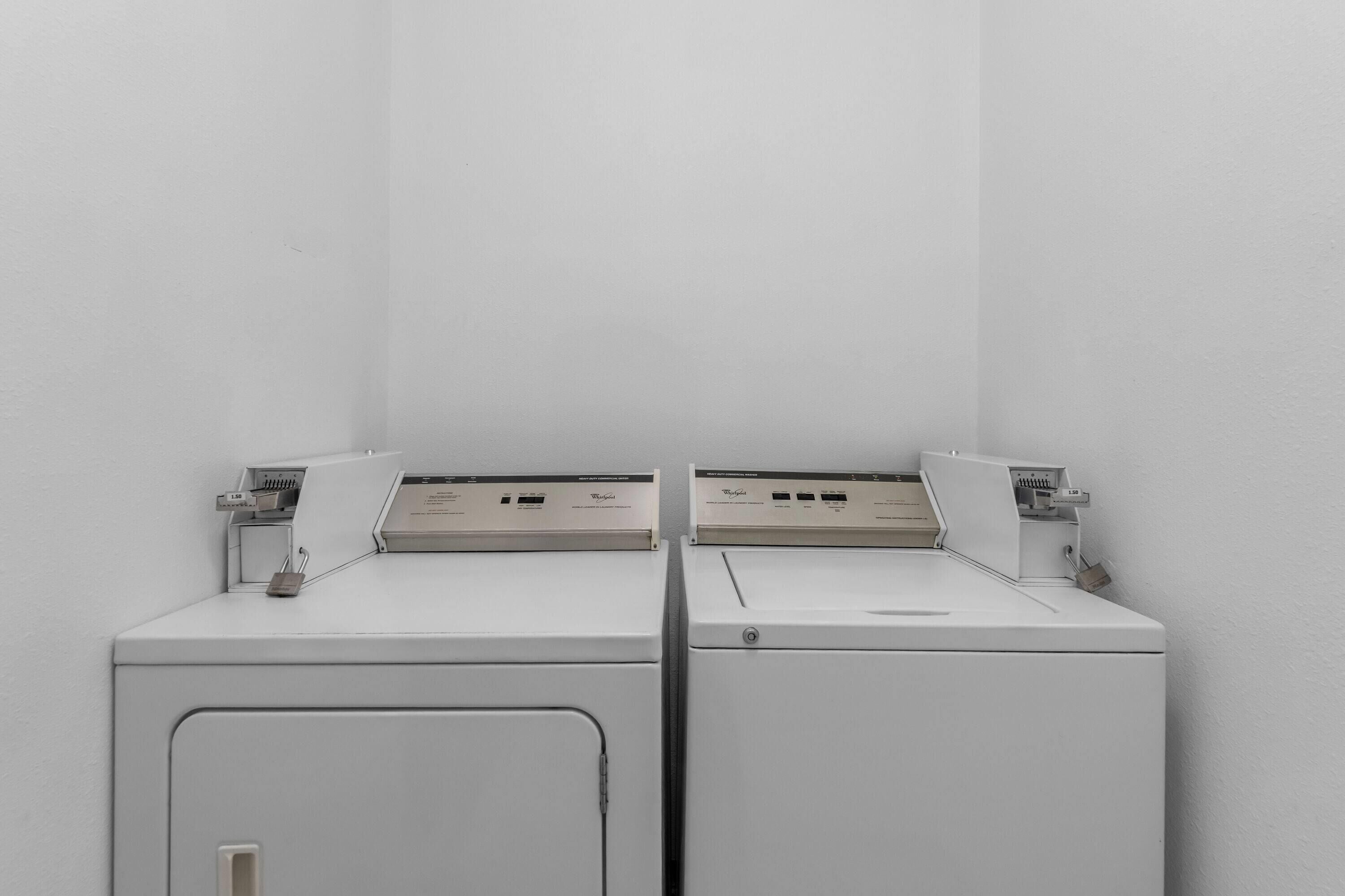 Two white front-loading washing machines in a corner with a plain wall.