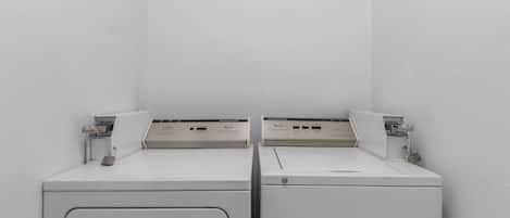 Two white front-loading washing machines in a corner with a plain wall.