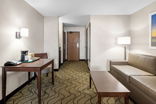 Ein Hotelzimmer mit Holztisch, einer Couch, einem Teppich mit Muster sowie einer Tür und einer Lampe.