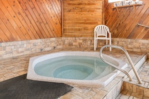 Un jacuzzi con revestimiento de piedra, una silla blanca y paredes de madera.
