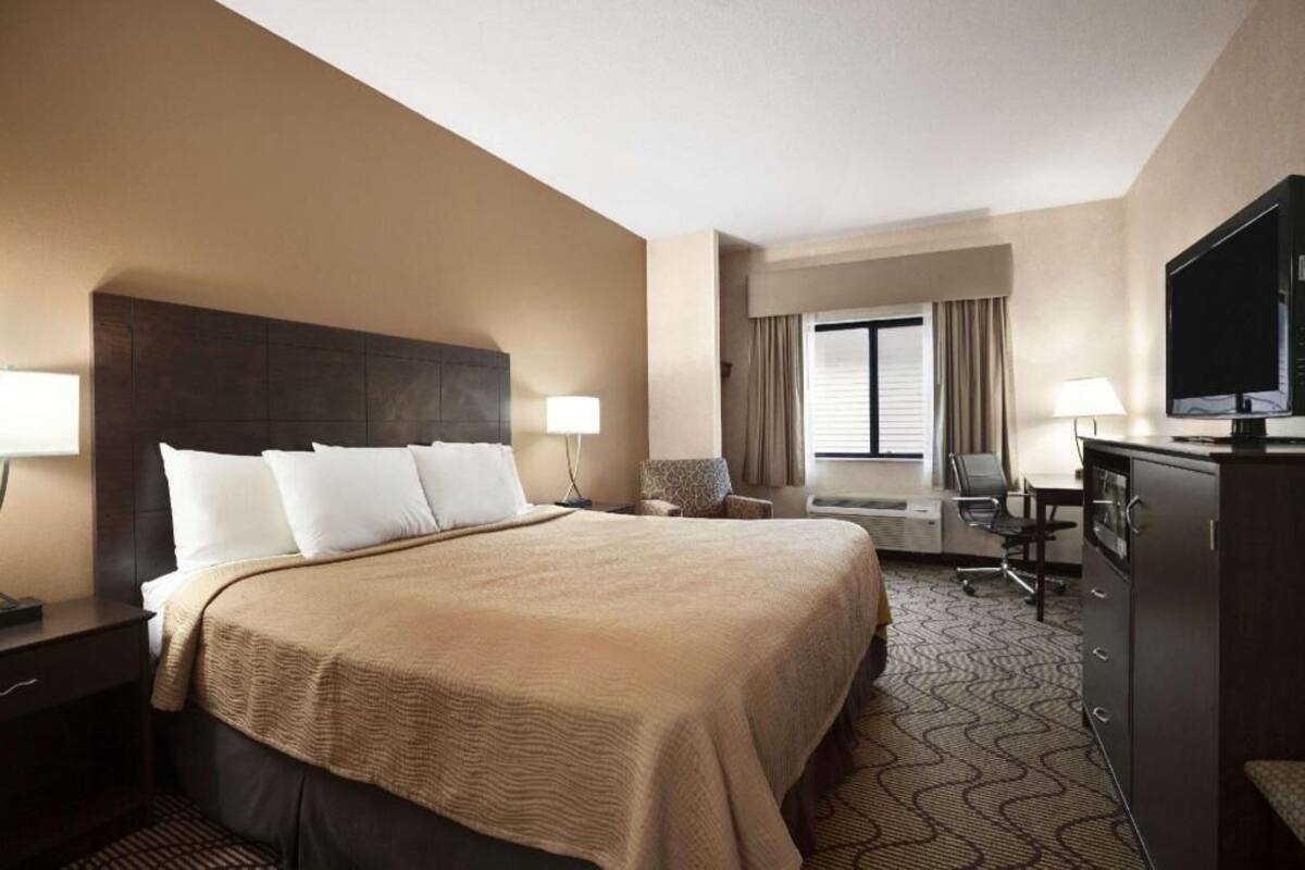 Habitación de hotel con una cama grande, un escritorio, un televisor y una ventana con cortinas.
