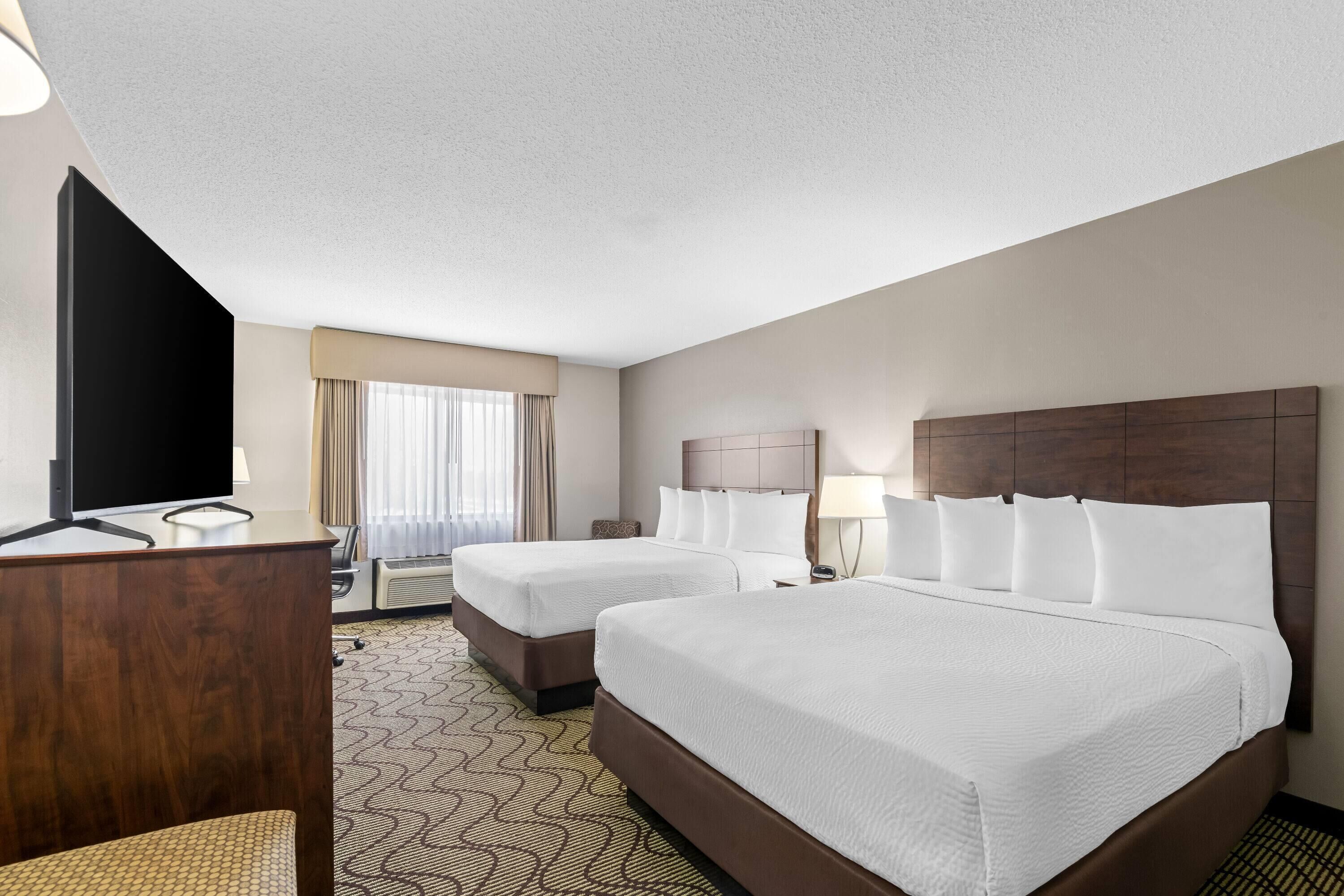A hotel room with two beds, a desk, a television, and a window with curtains.
