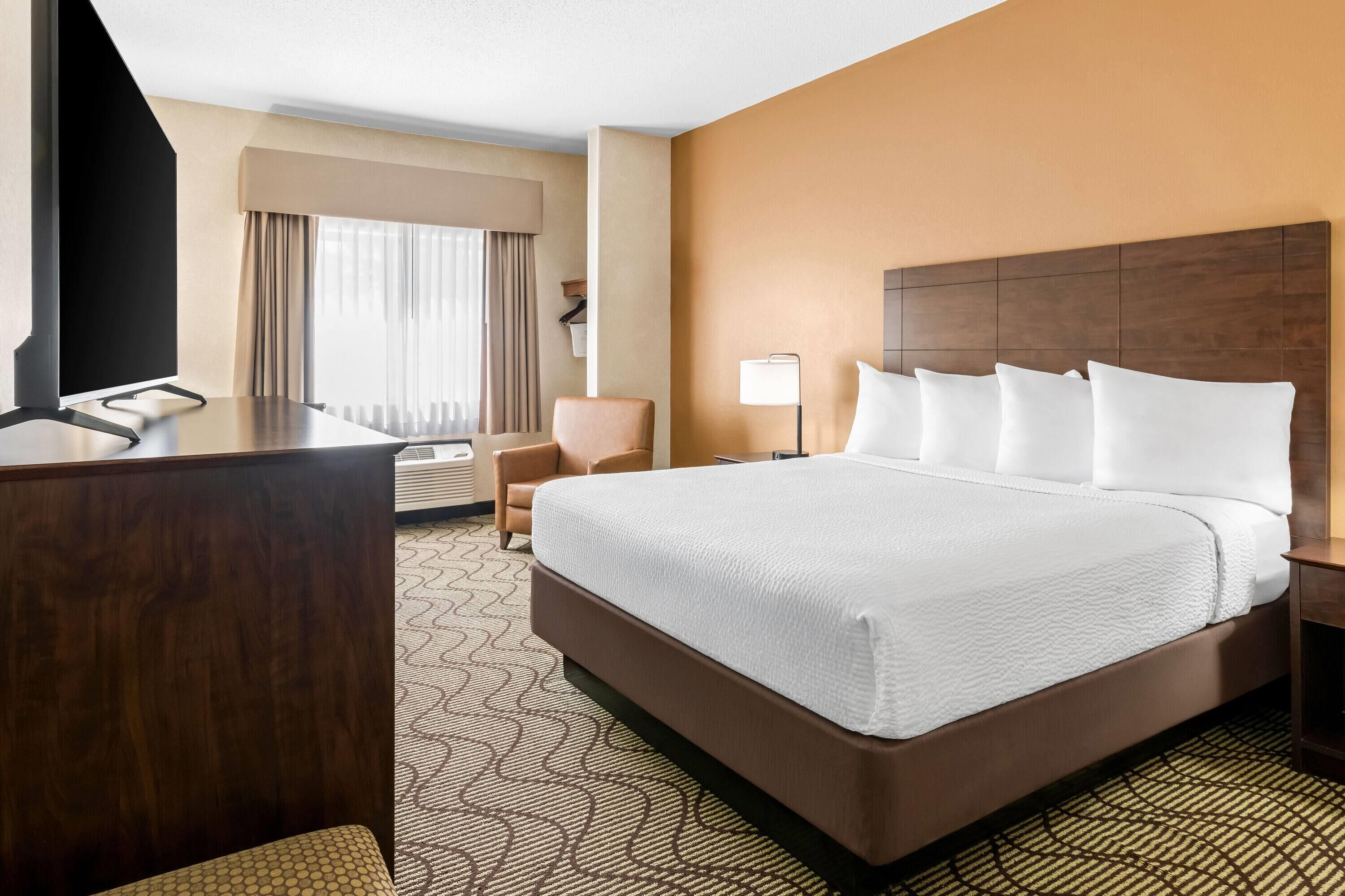 A hotel room with a large bed, a desk, a chair, a lamp, and a window with curtains.