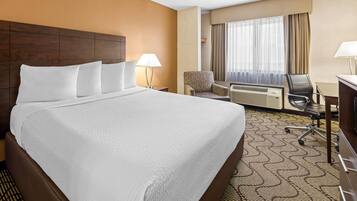 A hotel room with a large bed, a desk, a chair, a lamp, and an air conditioning unit.