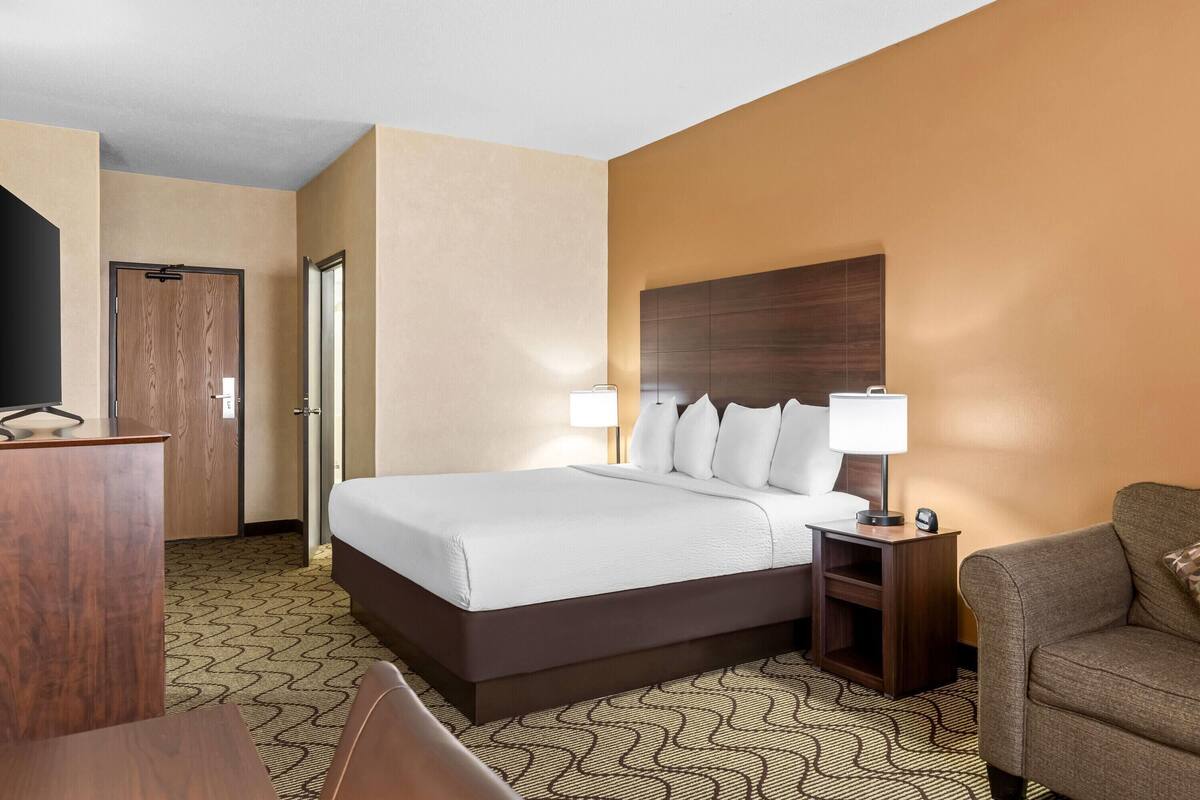 Una habitación de hotel con cama, mesita de noche, lámpara y escritorio con silla.
