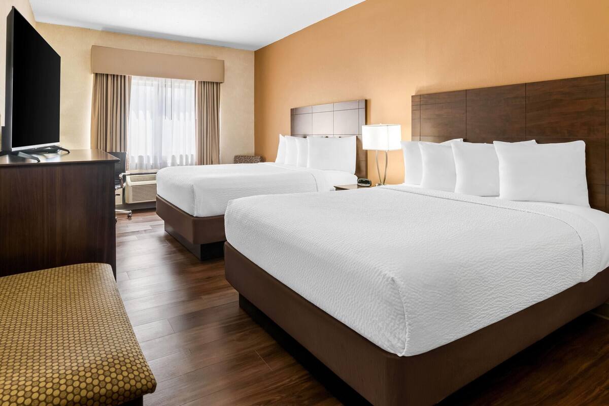 Una habitación de hotel con dos camas, un escritorio, un televisor y una ventana con cortinas.