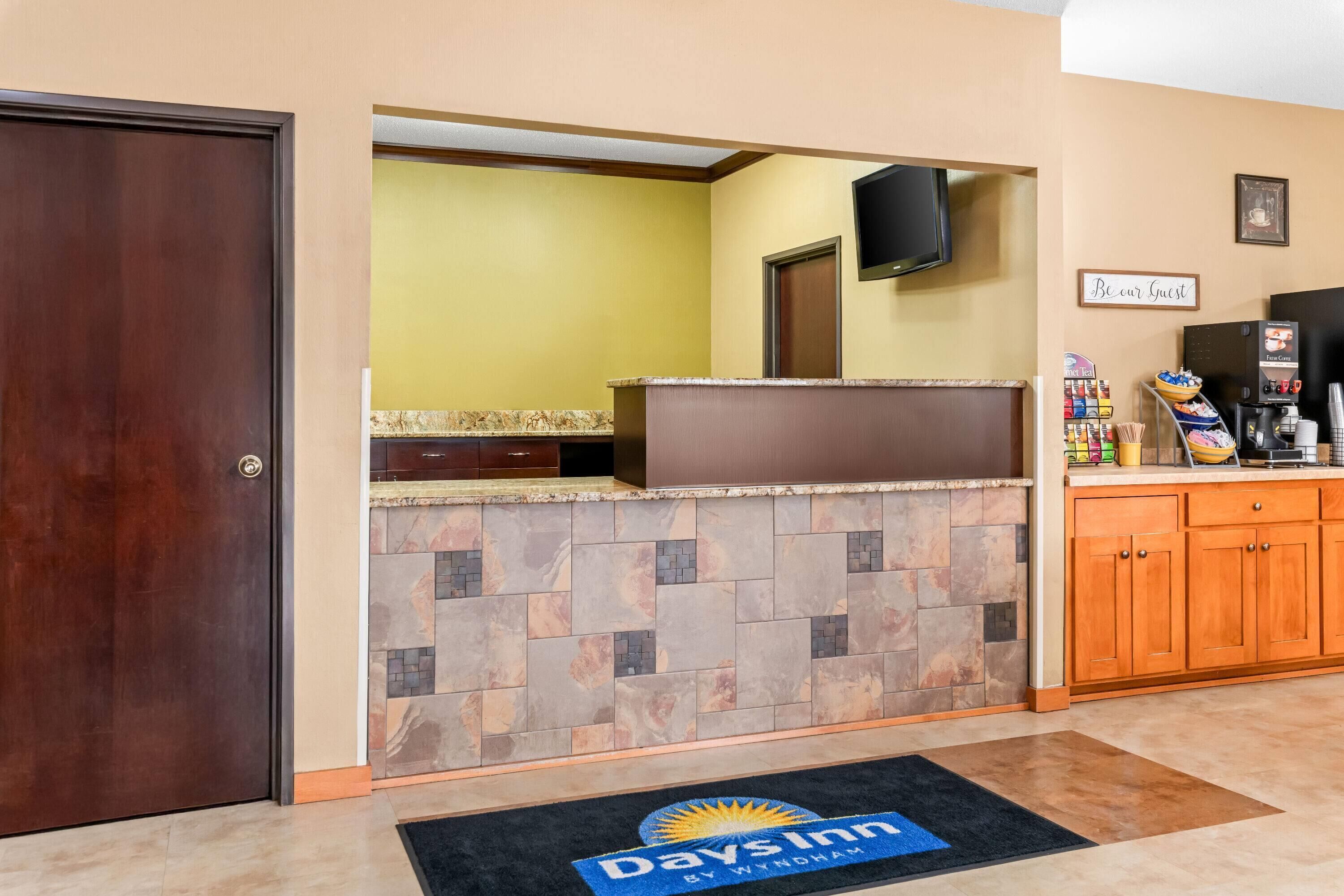 A reception area with a stone counter, wooden cabinets, a television, and a 'Be our Guest' sign.