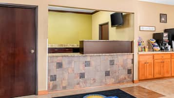 Un área de recepción con mostrador de piedra, armarios de madera, un televisor y un cartel que dice 'Be our Guest'.