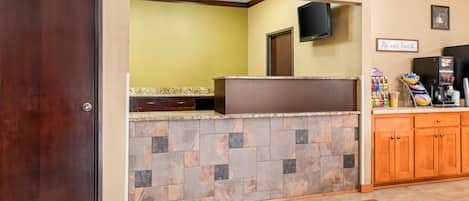 A reception area with a stone counter, wooden cabinets, a television, and a 'Be our Guest' sign.