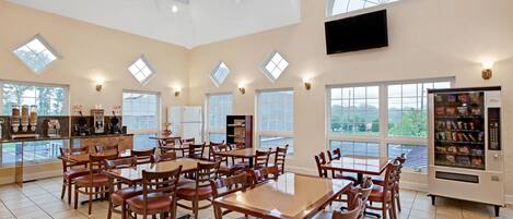 A spacious dining area with multiple tables and chairs, large windows, and a vending machine.