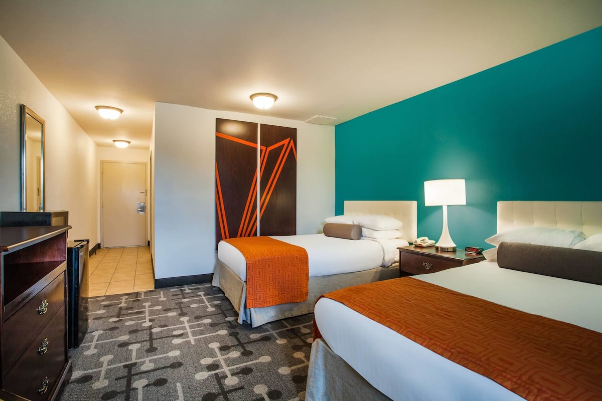 A hotel room with two beds, a desk, a dresser, and a bathroom door.