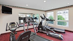 Een fitnessruimte met loopbanden, hometrainers en een televisiescherm.