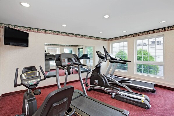 A gym with treadmills, stationary bikes, and a TV screen.