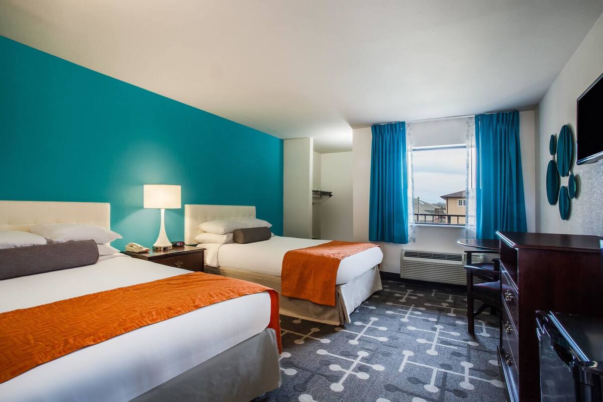 A hotel room with two beds, a desk, a chair, a TV, and a window with curtains.