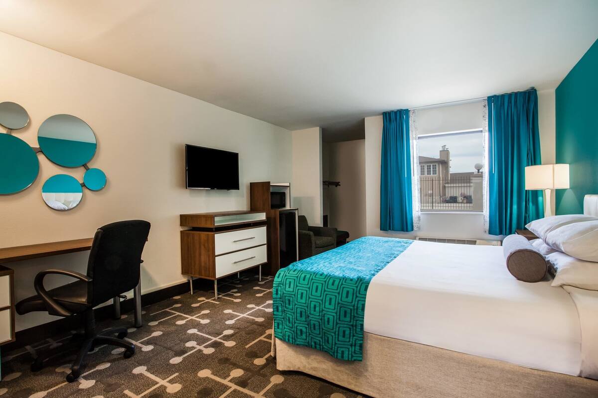 A hotel room with a bed, a desk, a chair, a TV, and a window with curtains.