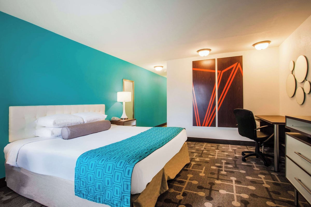 A hotel room with a bed, desk, chair, and a large window with curtains.