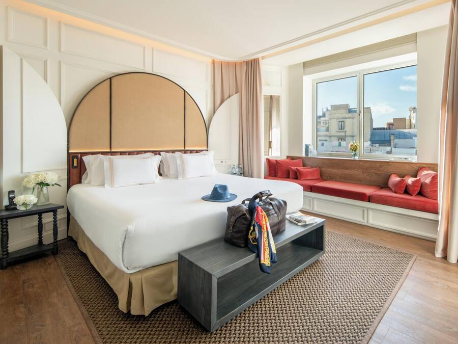 Habitación de hotel con una cama grande, un sofá, vista a la ciudad y una ventana con cortinas.