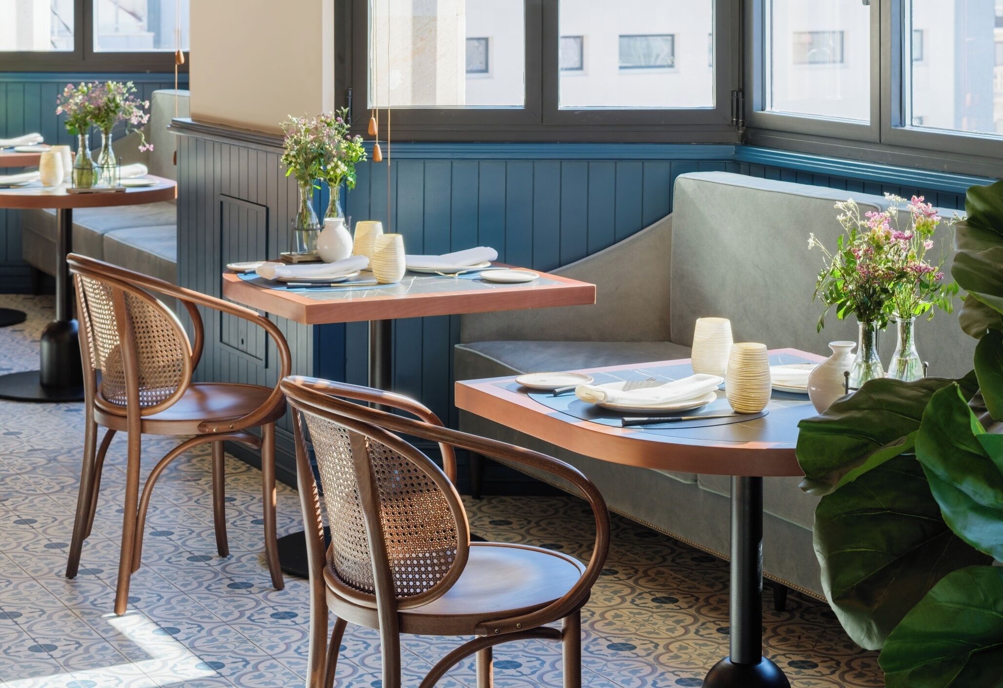 A restaurant interior with wooden tables and chairs, a bench, and floral centerpieces.