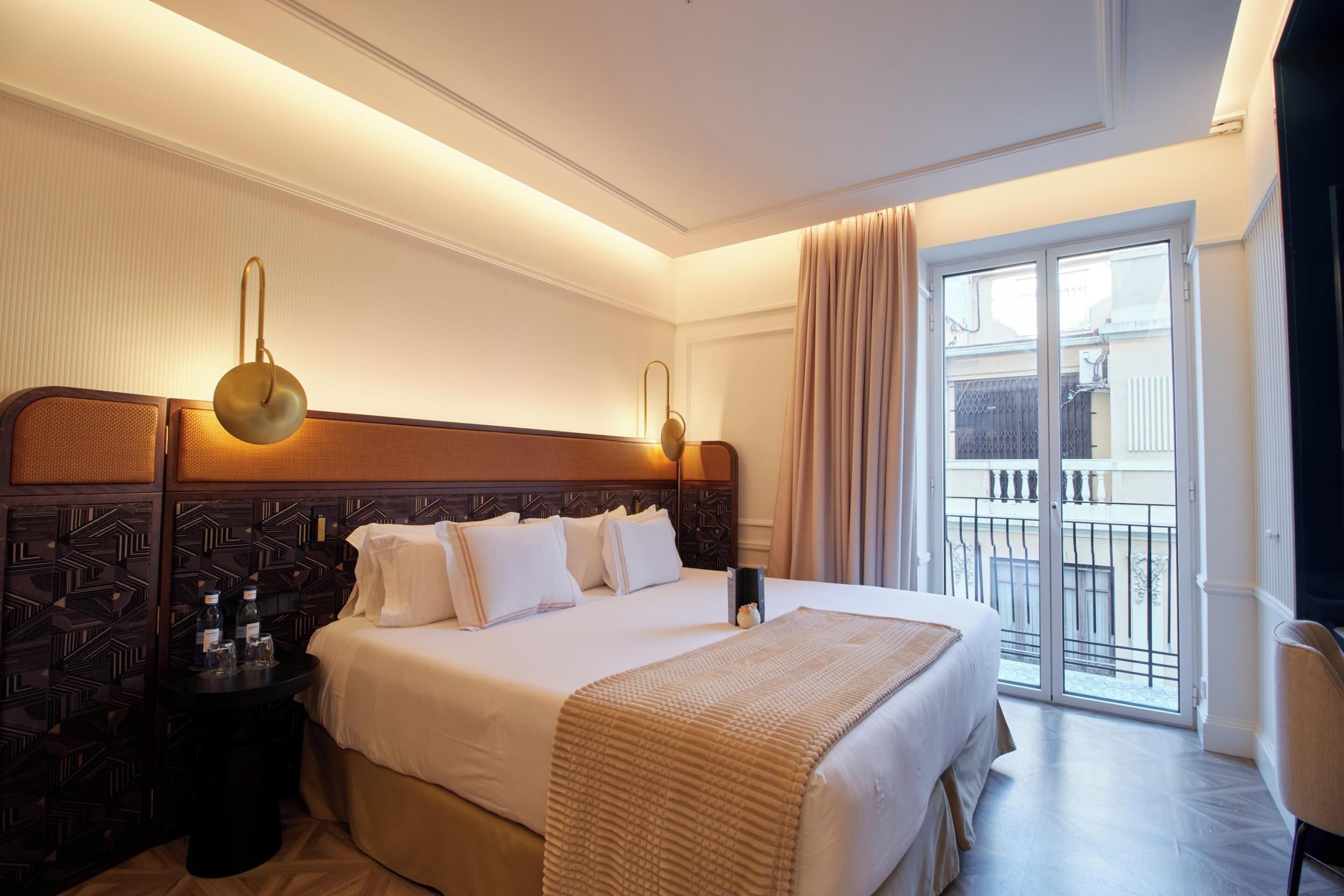 A hotel room with a large bed, a nightstand, a lamp, and a view of the outside balcony.
