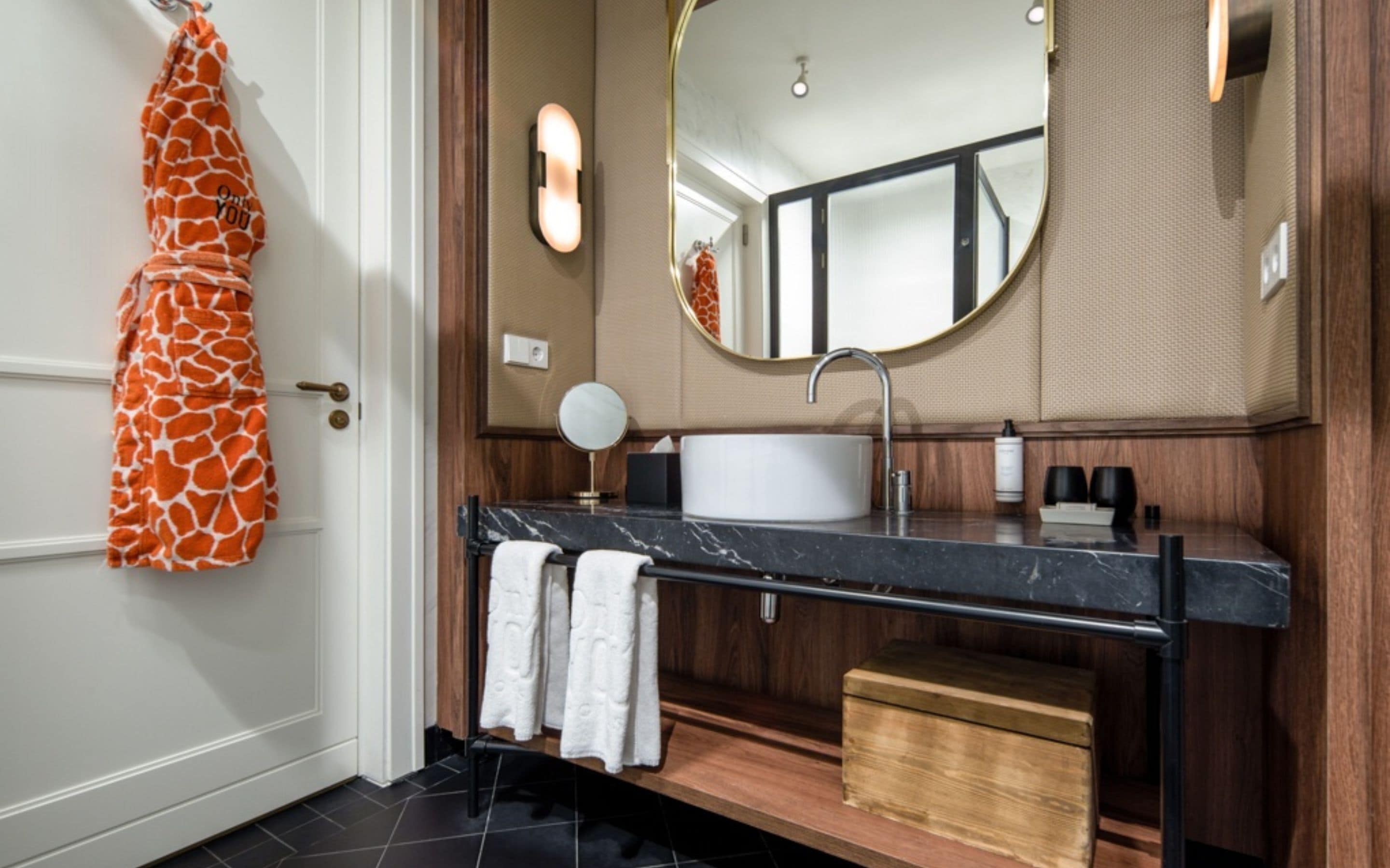 A bathroom with a marble sink, a round mirror, and a towel rack with a towel.