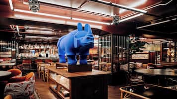 Interior de restaurante con una gran escultura de elefante azul sobre una mesa de madera, rodeado de sillas y mesas.