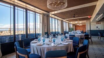 Un restaurante con mesas redondas dispuestas para comer, ventanas amplias que ofrecen vistas y una moderna lámpara de araña.