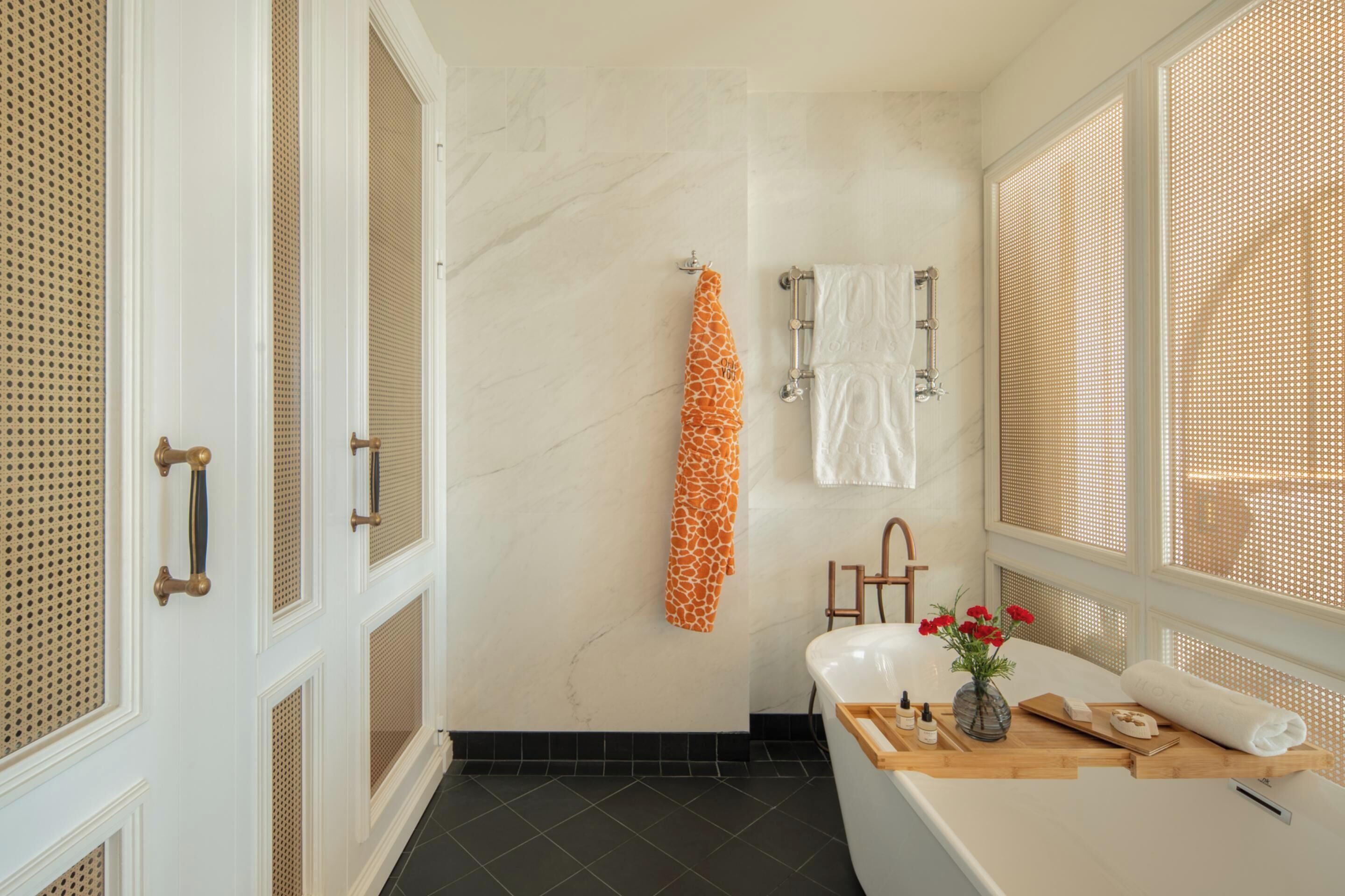 A bathroom with a bathtub, a sink, and a shower area. There are towels hanging on a rack, and a vase with flowers on the sink counter.